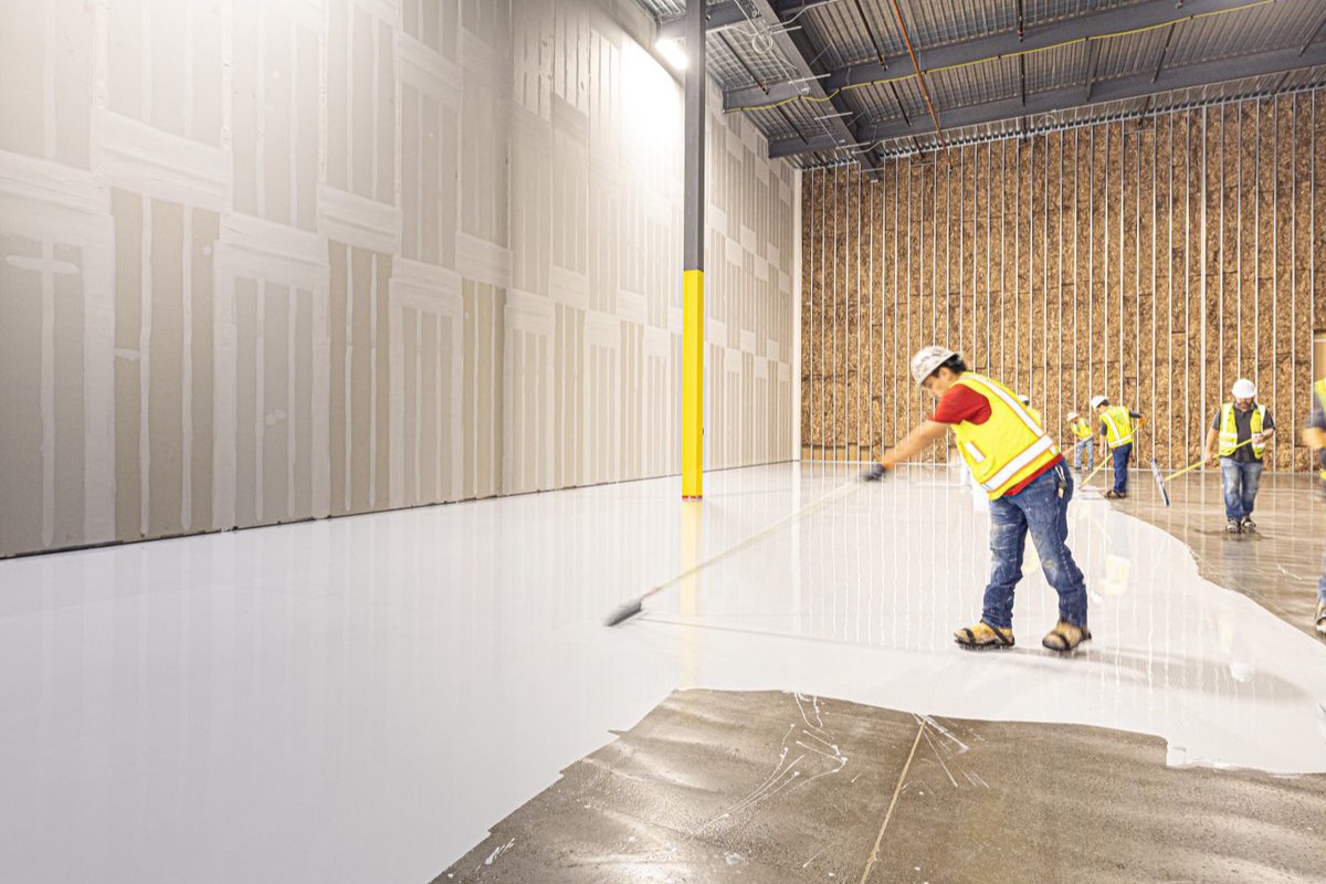 Workers in hi-vis laying a fresh resin floor across a large indoor slab